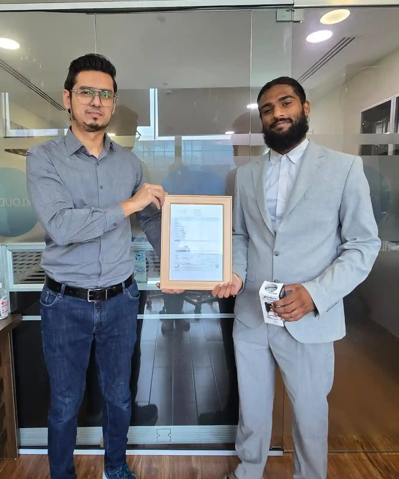 Two professionals at Kloudac, a leading Accounting firm, presenting a framed certificate and business materials in a modern office. This image highlights the success of a business setup in Dubai and the professional Accounting Services provided to local entrepreneurs.