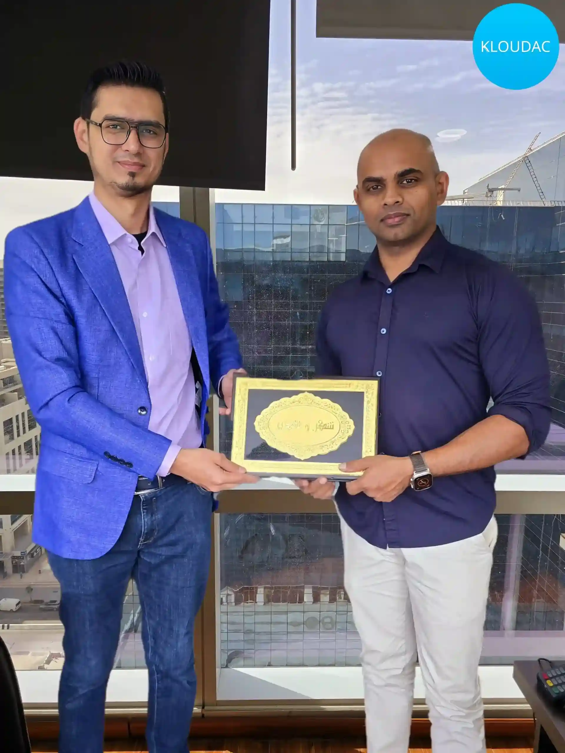 A professional consultant from Kloudac, a premier Accounting firm, presenting a framed business license to a smiling client. This successful business setup in Dubai highlights the expert Accounting Services provided to ensure a smooth transition for new entrepreneurs.