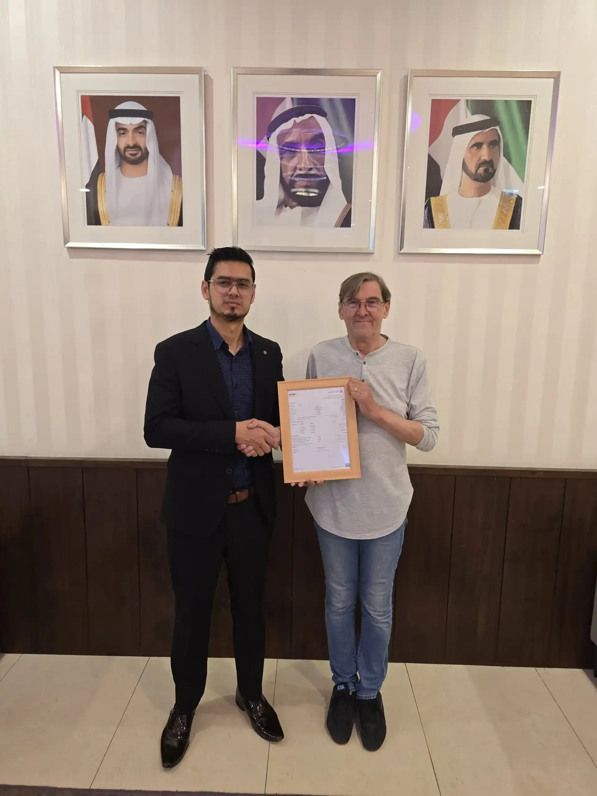 A Kloudac professional in a suit shaking hands with a client holding a framed certificate in an office featuring portraits of UAE leaders. This partnership exemplifies a successful business setup in Dubai supported by the premier Accounting Services of Kloudac, a top-rated Accounting firm.